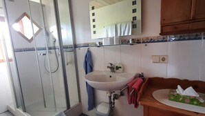 Ein Badezimmer mit einer Duschkabine aus Glas, einem Waschbecken mit Spiegel darüber und einem Holzschrank.