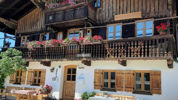 Ein traditionelles Holzhaus mit einem Balkon, der mit Blumen geschmückt ist, einer Holzbank davor und einem Schild, das ein Restaurant anzeigt.