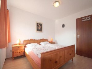 Ein Schlafzimmer mit einem hölzernen Bett, zwei Nachttischen mit Lampen, einer Wanduhr und einer Tür.