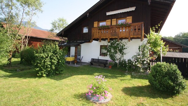 A traditional wooden house with a balcony, surrounded by a well-maintained garden with various plants and flowers. - Predigtstuhl vacation apartment in a rural setting, 55 m², 1 bedroom (Bayerisch Gmain)