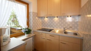 A kitchen with wooden cabinets, a double sink, and a window with curtains. - Predigtstuhl vacation apartment in a rural setting, 55 m², 1 bedroom (Bayerisch Gmain)