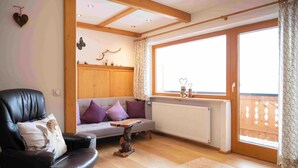 Ein gemütliches Wohnzimmer mit Ledersofa, Couchtisch aus Holz und Blick durch ein großes Fenster.