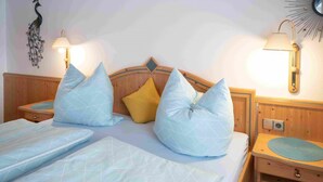 A double bed with two pillows, a wooden headboard, bedside tables with lamps, and a wall decoration. - One-room apartment Weitblick with shower/WC and balcony (Reit im Winkl)