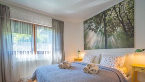 Une chambre à coucher avec un grand lit, un tableau représentant des arbres et une fenêtre avec des rideaux.