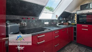 Eine moderne Küche mit roten Schränken, einer schwarzen Arbeitsplatte und einem Oberlicht.