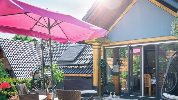 Ein Terrassenbereich im Freien mit Korbmöbeln, einem Schaukelstuhl und einem pinken Sonnenschirm.