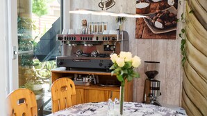 Ein gemütlicher Essbereich mit Kaffeemaschine, Tisch mit gemustertem Tischläufer und Blumen in einer Vase.