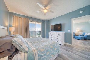 A bedroom with a bed, a ceiling fan, a dresser, a TV, and a balcony with a chair.