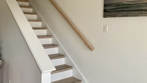 Una escalera con peldaños de madera y barandillas blancas que conduce a un rellano con un cuadro en la pared que muestra una escena de playa.