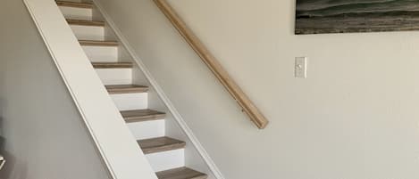 A staircase with wooden steps and white handrails, leading to a landing with a wall-mounted picture of a beach scene.