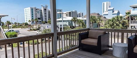 A wooden deck with outdoor furniture, overlooking a street with buildings and a clear sky.