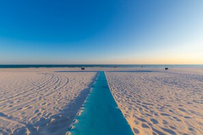 Ein Strand mit einem blauen Weg, der zum Wasser führt, blauem Himmel und Fußspuren im Sand.