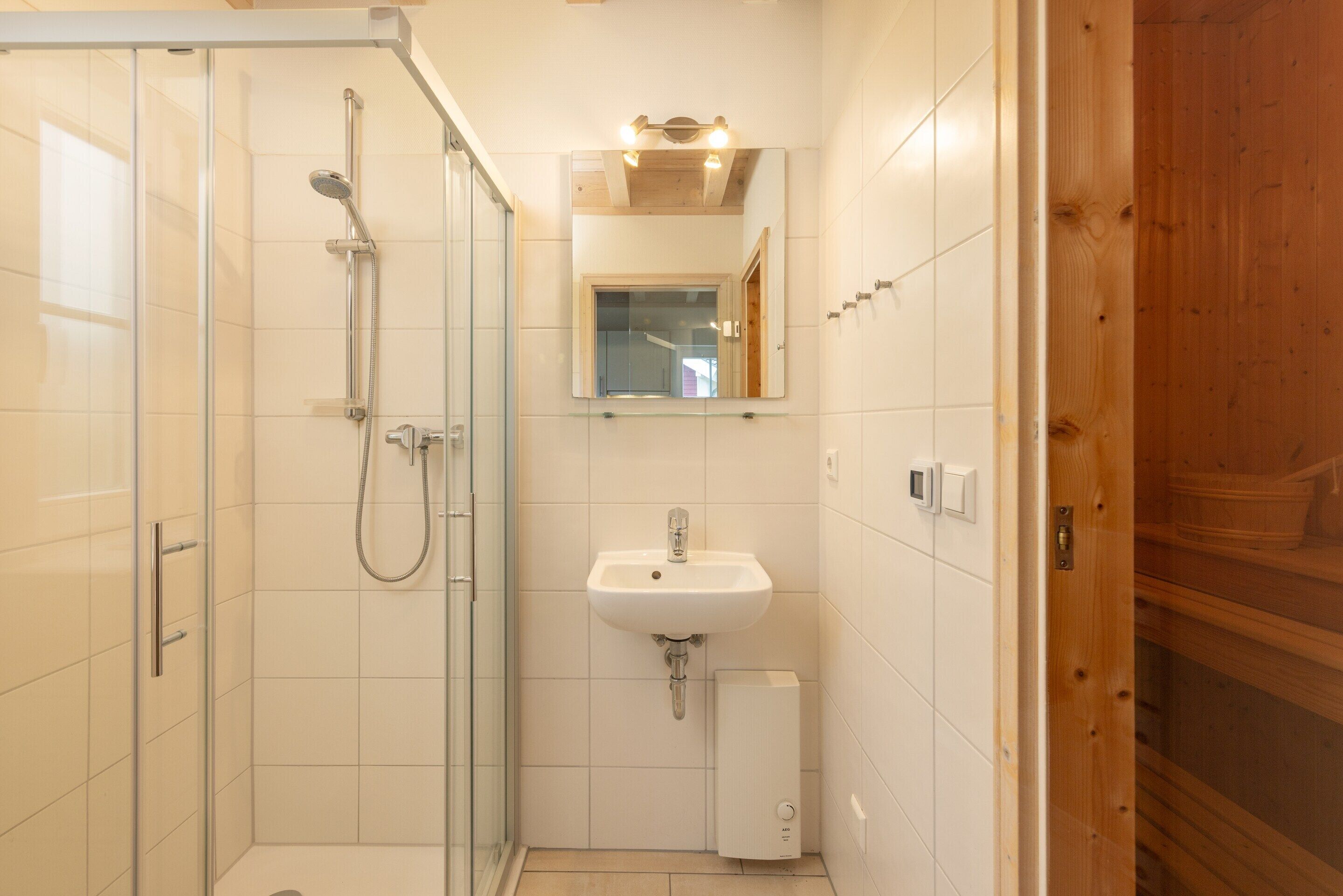 A bathroom with a glass shower enclosure, a sink, and a mirror above it.