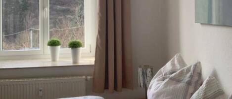 A bedroom with a bed, a window with curtains, and two potted plants on the windowsill.