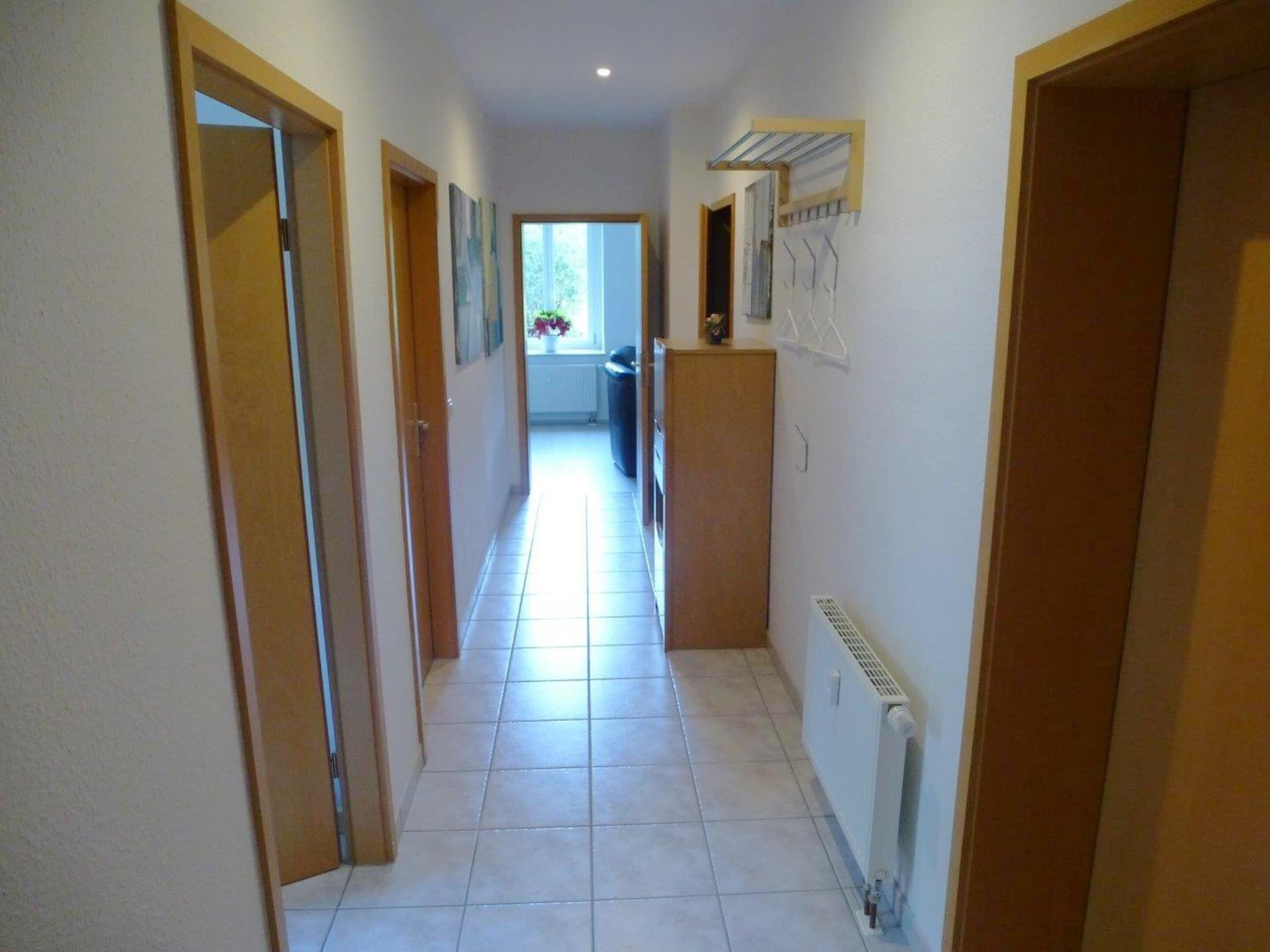 A narrow hallway with tiled flooring, wooden doors, and a radiator on the right.