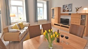 Una sala de estar acogedora con sofá, mesa de comedor, sillas, televisor, armarios de madera y una ventana con cortinas.