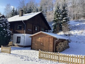 A wooden cabin with a sloped roof, a separate garage, and a snow-covered landscape. - Ferienwohnung in Kamschlacken (Osterode am Harz)