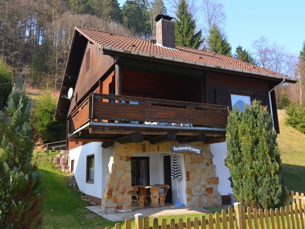 A chalet-style building with a stone facade, wooden balcony, and a sign indicating it is a guesthouse. - Ferienwohnung in Kamschlacken (Osterode am Harz)