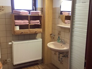 A small bathroom with a white radiator, a sink, and a shelf with folded towels. - Ferienwohnung in Kamschlacken (Osterode am Harz)