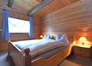 A wooden cabin bedroom with a bed, two bedside tables, and a window with curtains. - Ferienwohnung in Kamschlacken (Osterode am Harz)