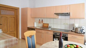 Cozinha compacta com armários de madeira, uma mesa de jantar com toalha xadrez e uma tigela de frutas sobre a mesa.