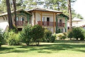 Un bâtiment à deux étages doté d’un balcon, entouré d’arbres et d’une pelouse.