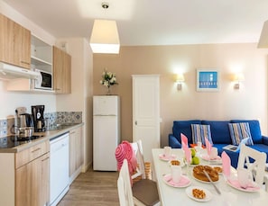 A compact kitchen with modern appliances, a dining area with a table set for two, and a blue sofa in the living area. - Apartment in La Baule Near Cote D'amour (Pornichet)