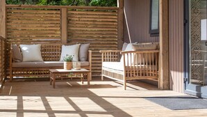 Een houten terras met een bank en stoelen, een kleine tafel en een bloempot.