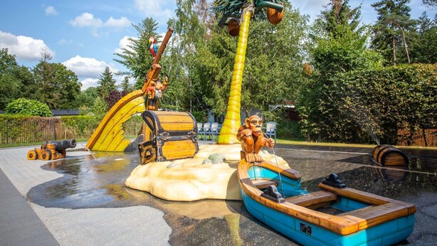Een speelplaats met water, een piratenschip, een palmboom en een papegaai.