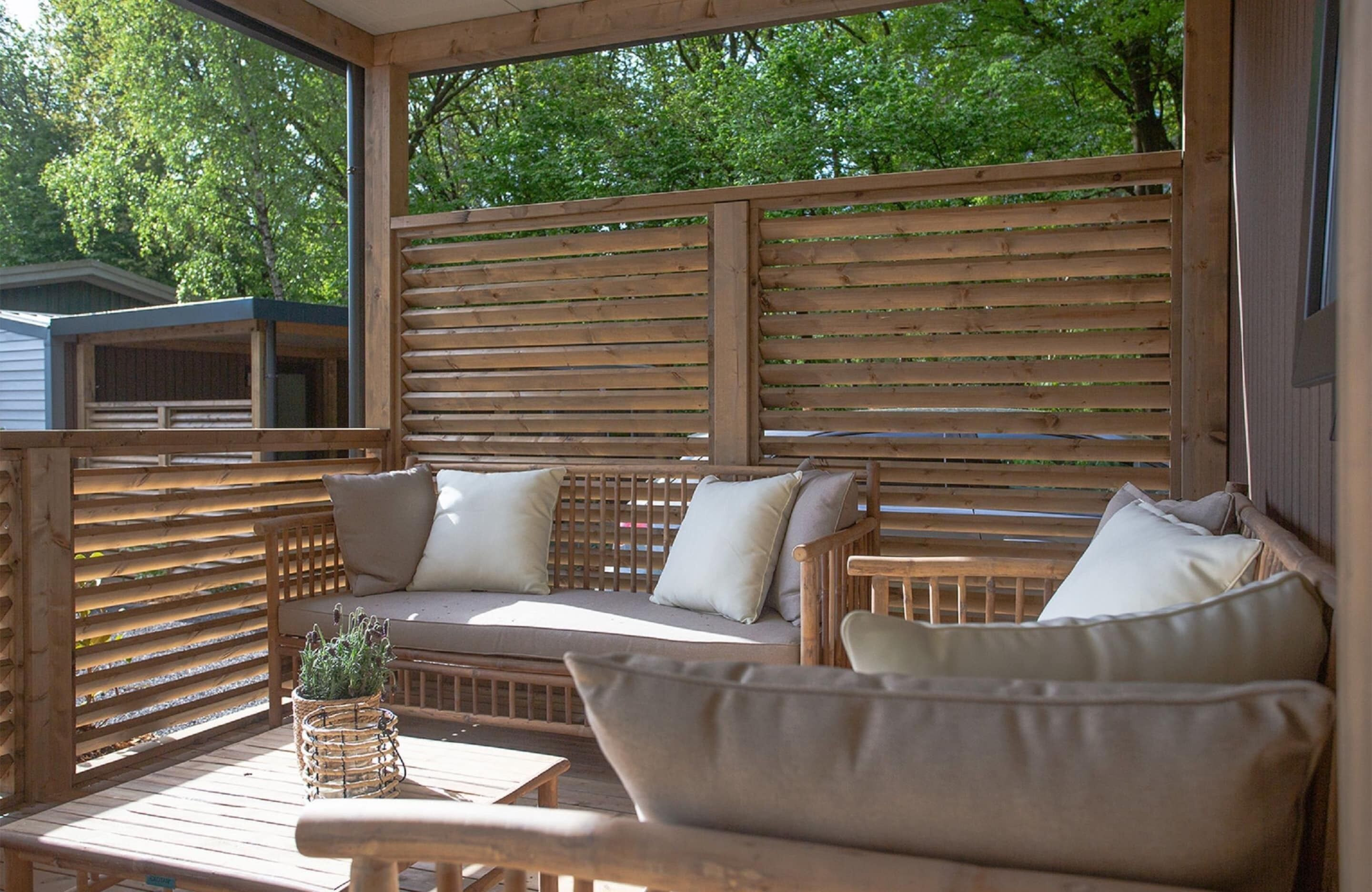 Una terraza de madera con un sofá, sillas, una mesita y una planta en maceta.