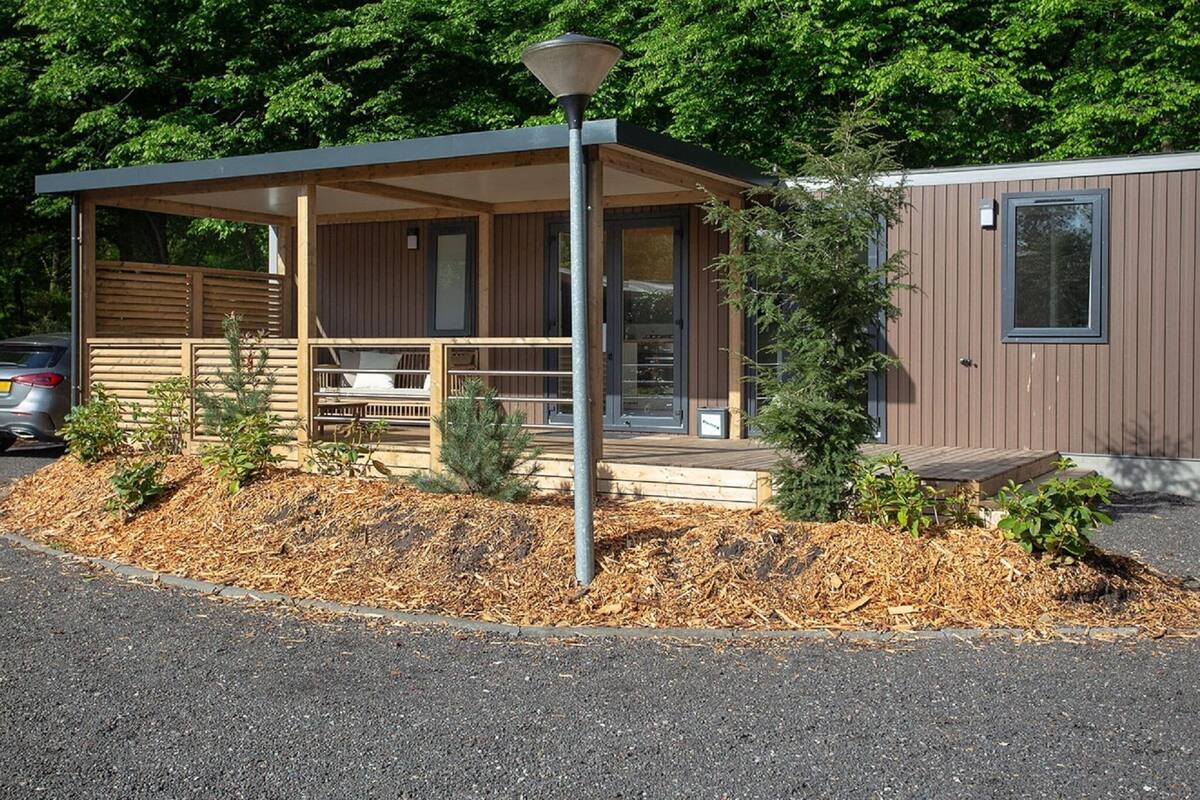 A modern cabin with a covered porch, a small deck, and a compact structure with a window.