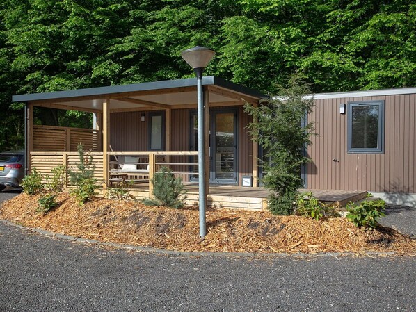 A modern cabin with a covered porch, a small deck, and a compact structure with a window.