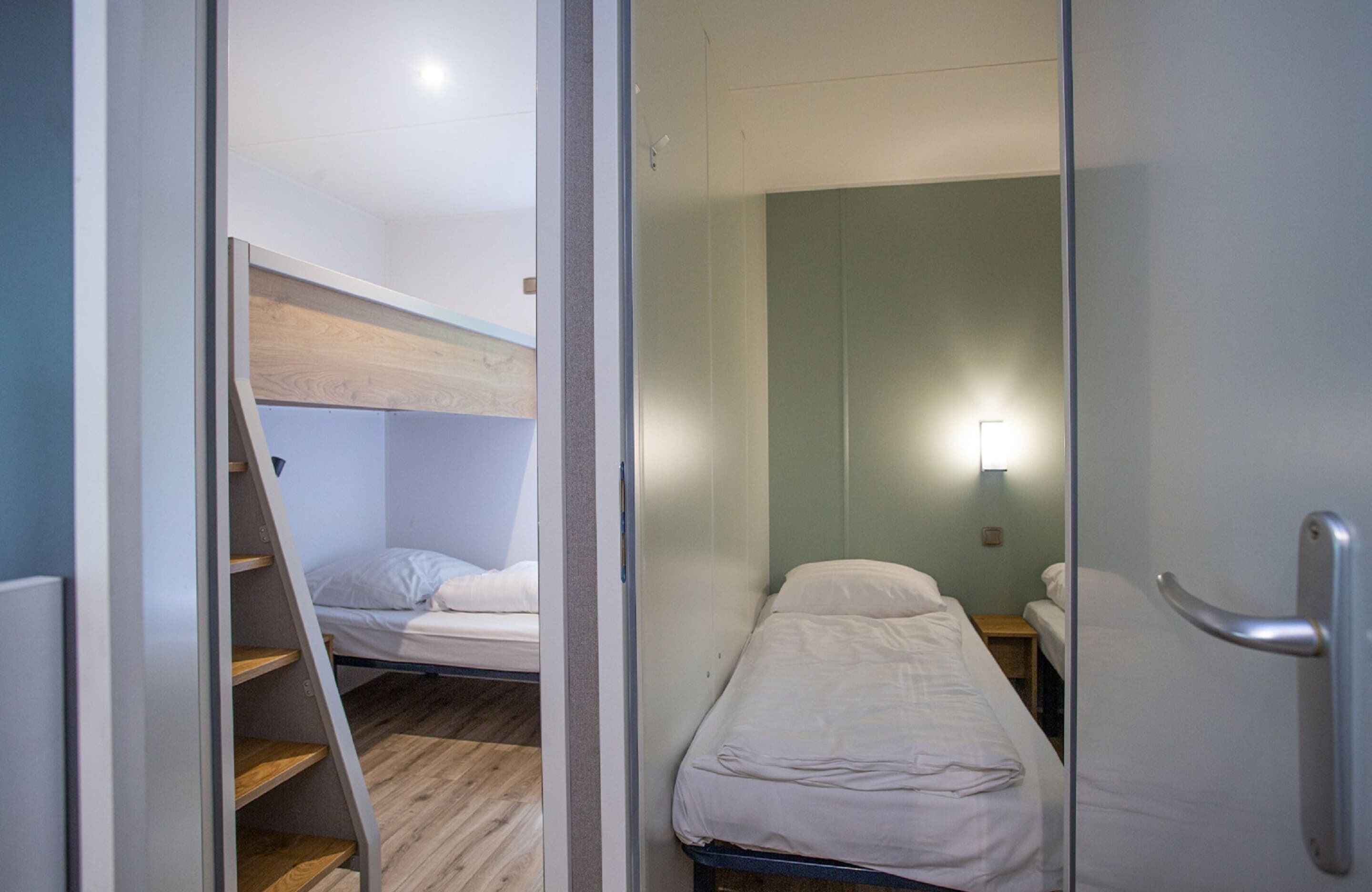 Una habitación pequeña con una cama litera, una mesita de noche y una cama individual.