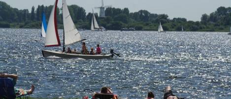 A lake with sailboats and people relaxing on the shore.