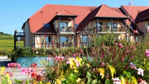 A multi-story building with a red-tiled roof, balconies with railings, and a garden in the foreground. - Apartment in Bergheim Near Picturesque Town (Bergheim)