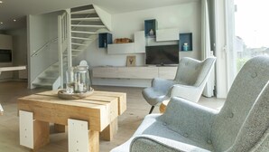 A modern living room with a staircase, a wooden coffee table, and a grey armchair. - Villa in Cadzand Near Beach & Dunes (Cadzand-Bad)
