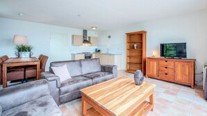 Un salon comprenant un canapé, une table basse, un téléviseur, un meuble en bois et un coin repas avec une table et des chaises.
