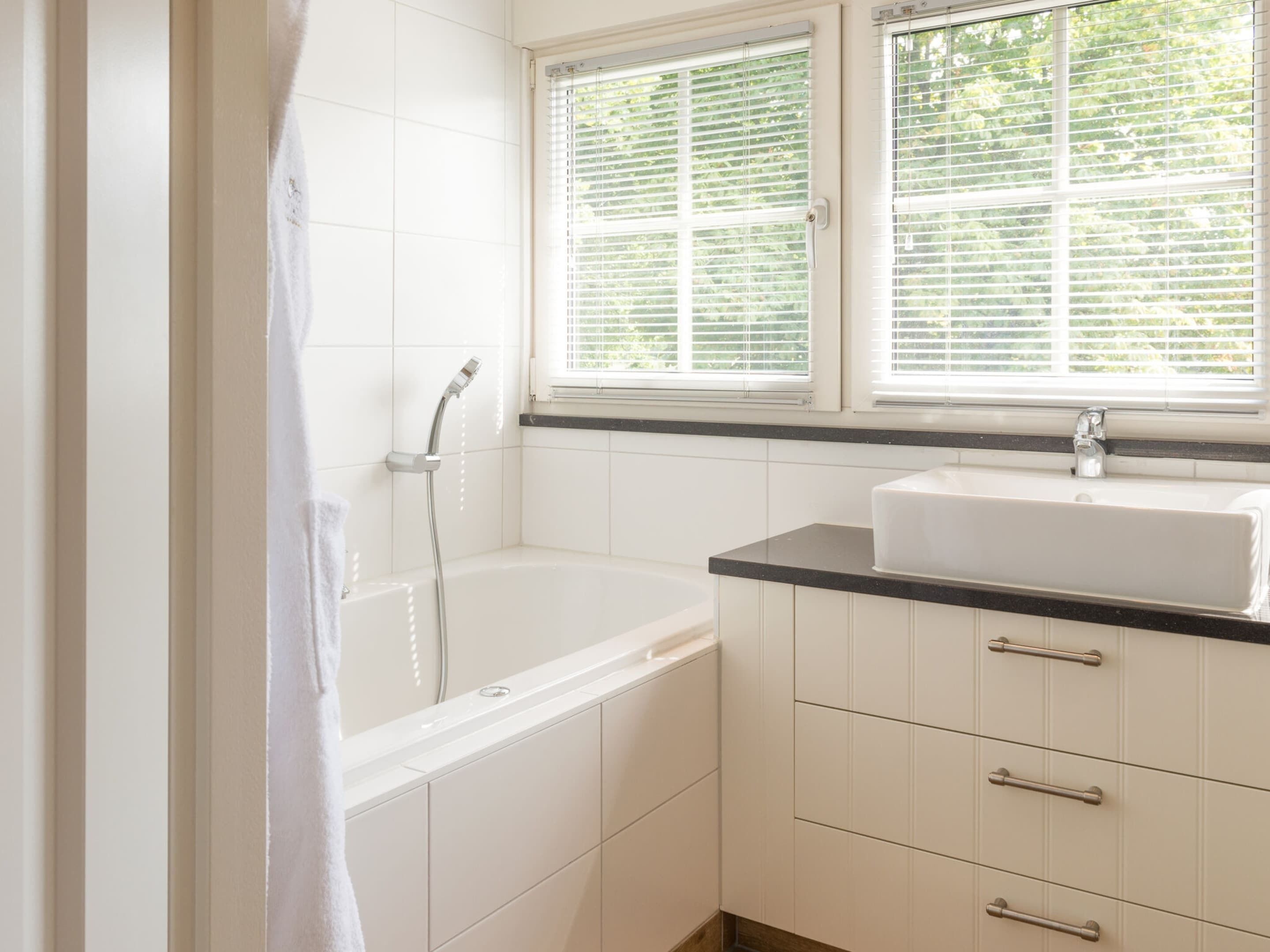 A bathroom with a bathtub, a sink, and a window with blinds.