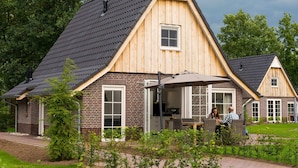 Une maison en bois avec un toit en pente, une façade en briques et un patio aménagé avec des meubles d’extérieur.