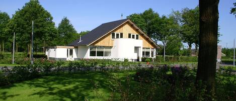 A modern two-story house with a sloped roof, surrounded by a well-maintained garden with pink flowers.