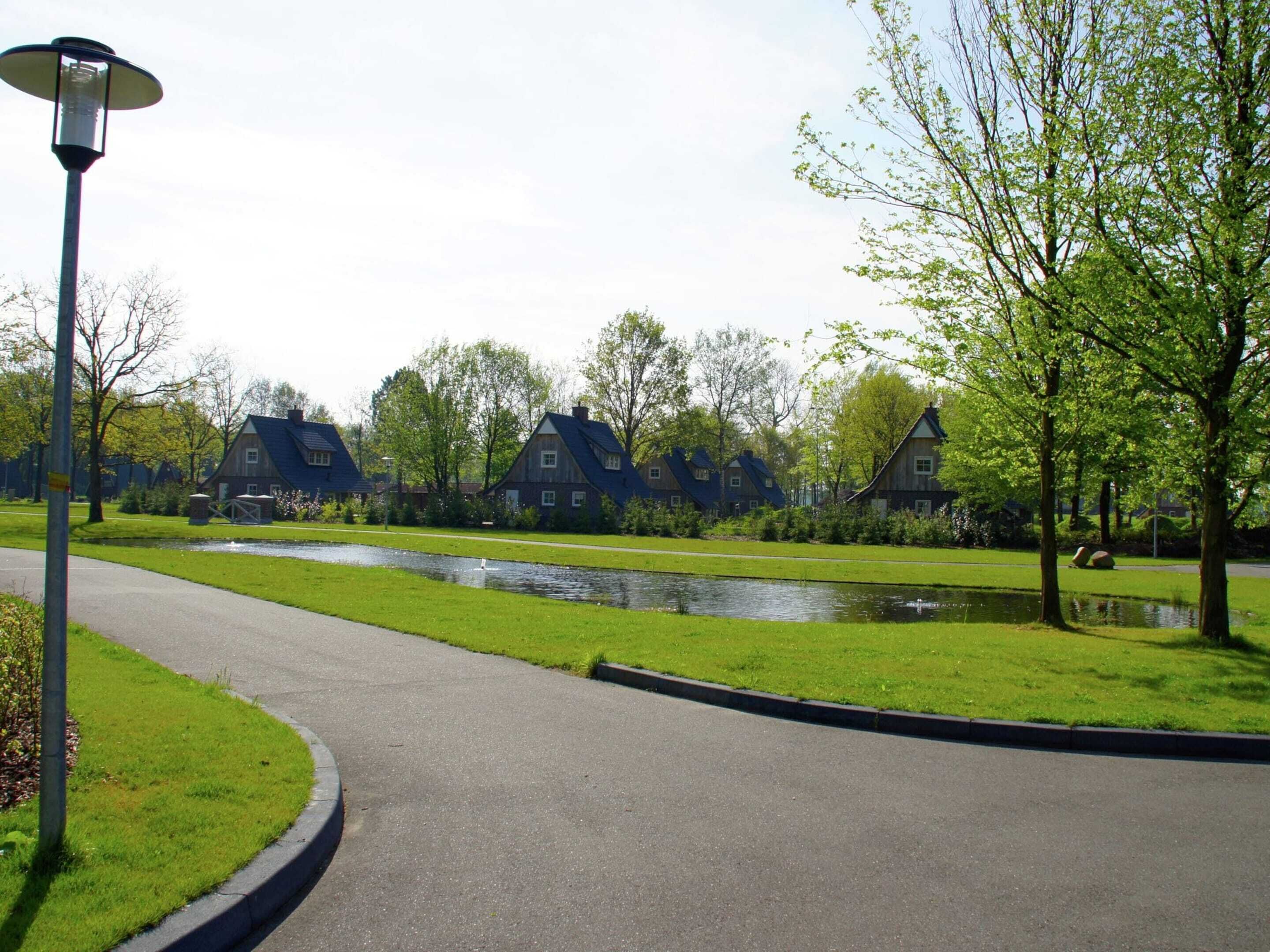 A pathway curving through a park with a pond, surrounded by traditional houses with sloped roofs.