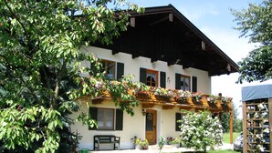 Ein traditionelles Chalet mit Balkon, der mit Blumen geschmückt ist, einer Holzbank und einem gepflegten Rasen.