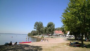 Ein Strand mit einer Reihe Liegestühle und Sonnenschirmen, einem roten Kajak und einem Gebäude mit rotem Dach im Hintergrund.