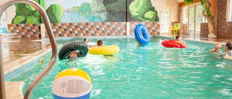 An indoor swimming pool with clear water, surrounded by a tiled wall with a mural of trees and a brick wall.