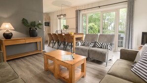 A modern living room with a wooden coffee table, grey sofa, and a dining area with chairs. - Thatched Villa in National Park (Paasloo)