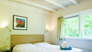A hotel room with a bed, a window with curtains, a framed picture on the wall, and a bedside table with books. - Charming Haystack Stay (Dwingeloo)