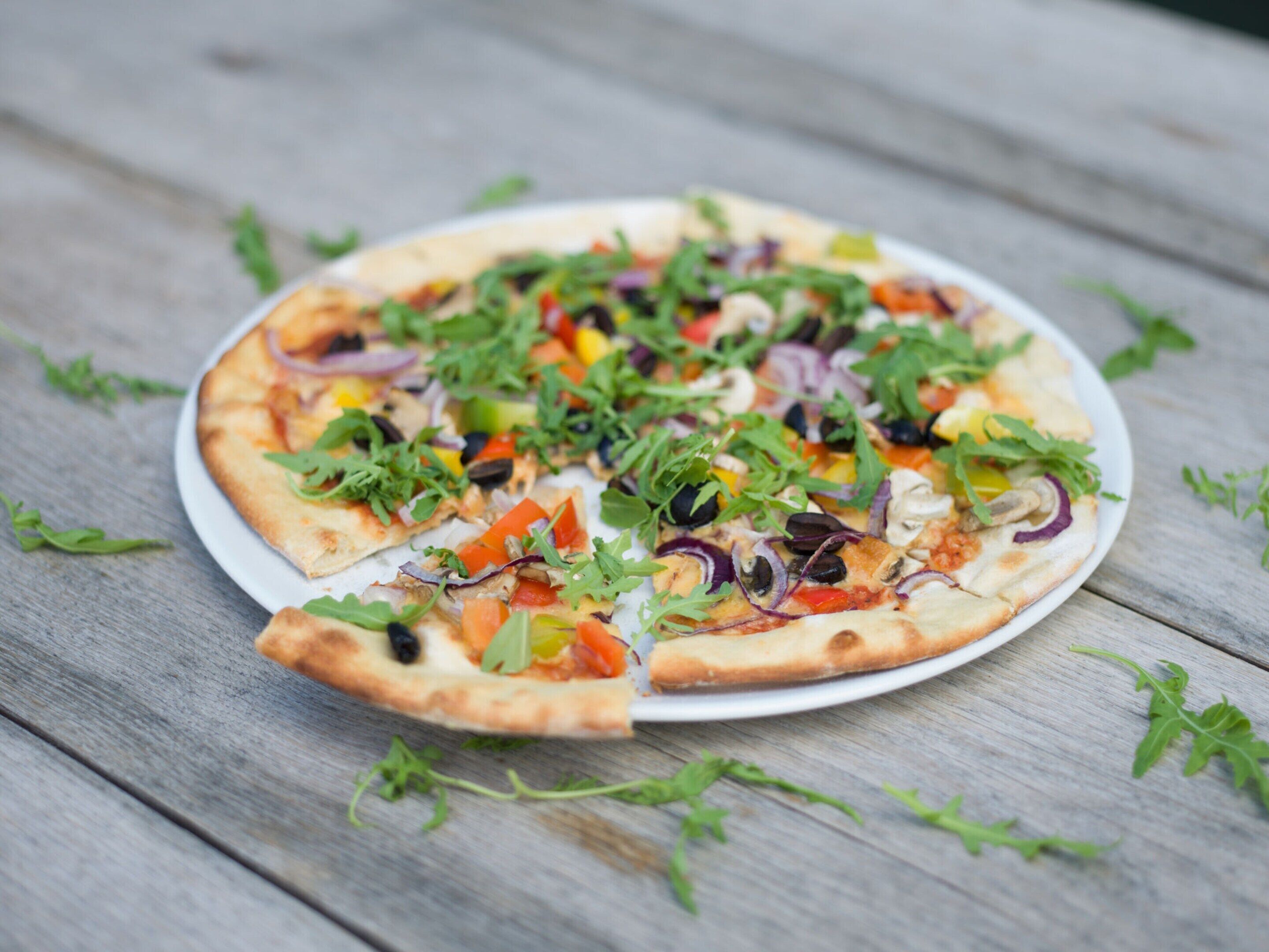 A pizza on a white plate with various toppings, placed on a wooden table.