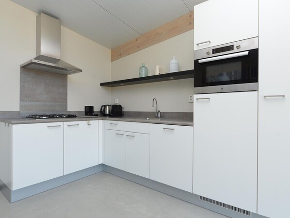 Una cocina moderna con armarios blancos, una campana extractora de acero inoxidable, un microondas y una cafetera.