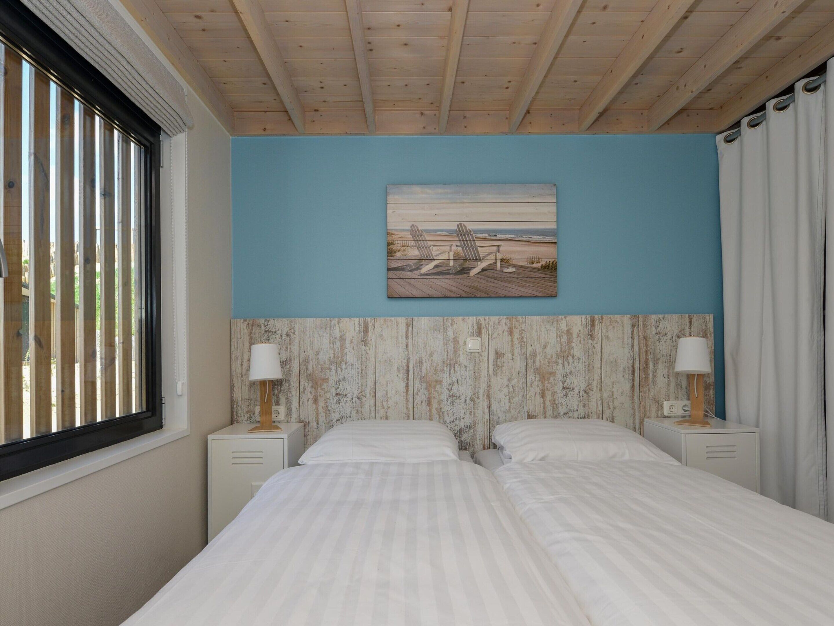 Ein Schlafzimmer mit zwei Betten, einer Holzbalkendecke, einer blauen Wand und einem Gemälde mit einer Strandansicht.
