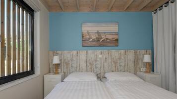 A bedroom with two beds, a wooden ceiling, a blue wall, and a beach scene painting.